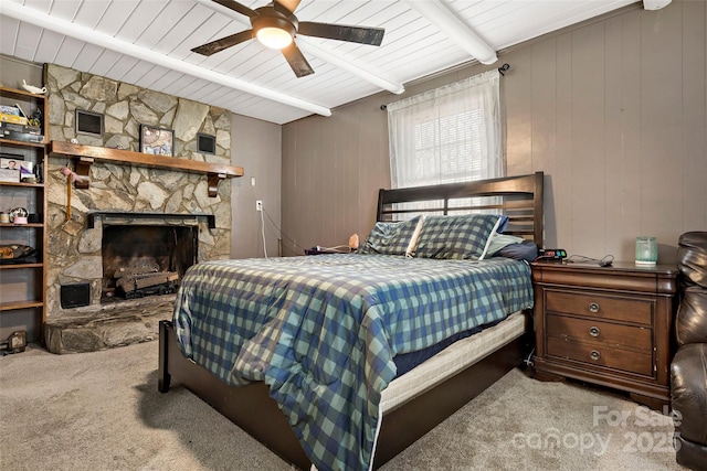 bedroom with beamed ceiling, a stone fireplace, carpet flooring, and ceiling fan