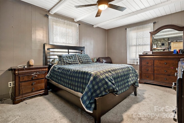 carpeted bedroom with ceiling fan, beam ceiling, and wood walls