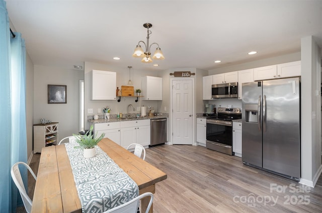 kitchen with appliances with stainless steel finishes, sink, white cabinets, hanging light fixtures, and light stone counters