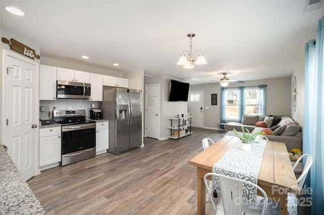 kitchen with decorative light fixtures, light hardwood / wood-style flooring, appliances with stainless steel finishes, ceiling fan with notable chandelier, and white cabinets