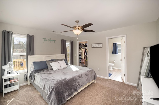 bedroom with ensuite bath, a spacious closet, light colored carpet, a closet, and ceiling fan