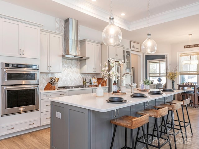 kitchen with wall chimney range hood, appliances with stainless steel finishes, a kitchen breakfast bar, a spacious island, and decorative light fixtures