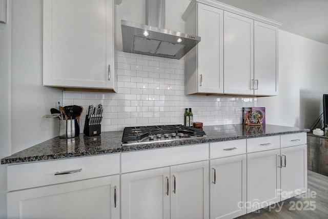 kitchen featuring white cabinetry, dark stone countertops, backsplash, stainless steel gas cooktop, and wall chimney exhaust hood