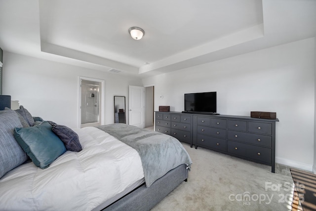 carpeted bedroom featuring a raised ceiling and ensuite bathroom