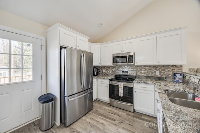 kitchen featuring stainless steel appliances, white cabinetry, vaulted ceiling, and decorative backsplash