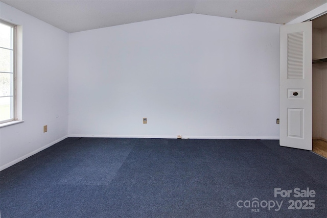 spare room featuring dark colored carpet and vaulted ceiling