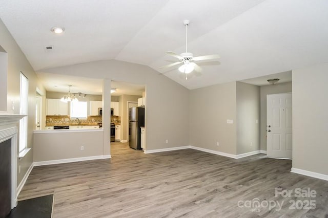 unfurnished living room featuring vaulted ceiling, wood-type flooring, and ceiling fan with notable chandelier