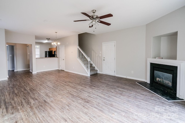 unfurnished living room featuring ceiling fan with notable chandelier and hardwood / wood-style floors