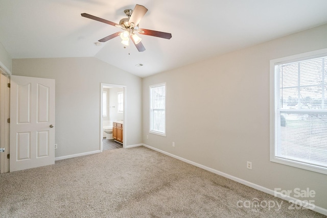 unfurnished bedroom featuring light colored carpet, lofted ceiling, connected bathroom, and multiple windows