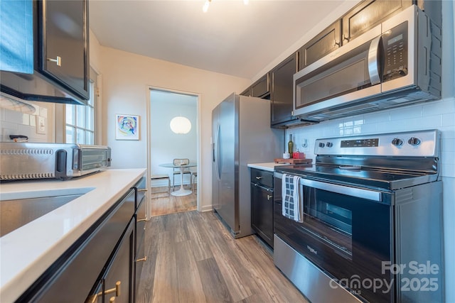 kitchen featuring hardwood / wood-style flooring, appliances with stainless steel finishes, backsplash, and decorative light fixtures