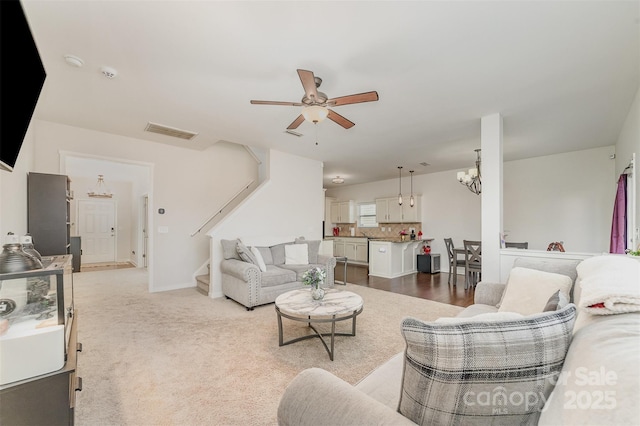 living area with stairway, visible vents, light colored carpet, and ceiling fan with notable chandelier