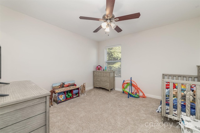 bedroom featuring a nursery area, light colored carpet, ceiling fan, and baseboards