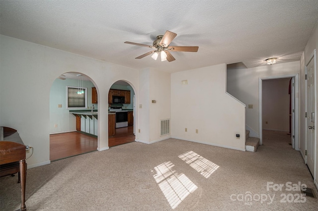 unfurnished living room with ceiling fan, light colored carpet, and a textured ceiling