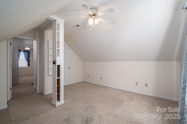 additional living space featuring vaulted ceiling, ceiling fan, light carpet, and a textured ceiling