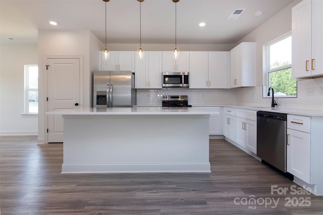 kitchen featuring a kitchen island, white cabinets, light countertops, appliances with stainless steel finishes, and hanging light fixtures