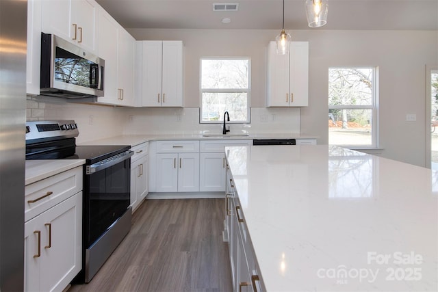 kitchen featuring light stone counters, appliances with stainless steel finishes, white cabinets, and a sink