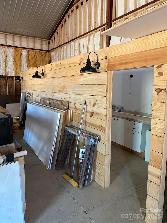 interior space featuring concrete flooring, vaulted ceiling, and wood walls