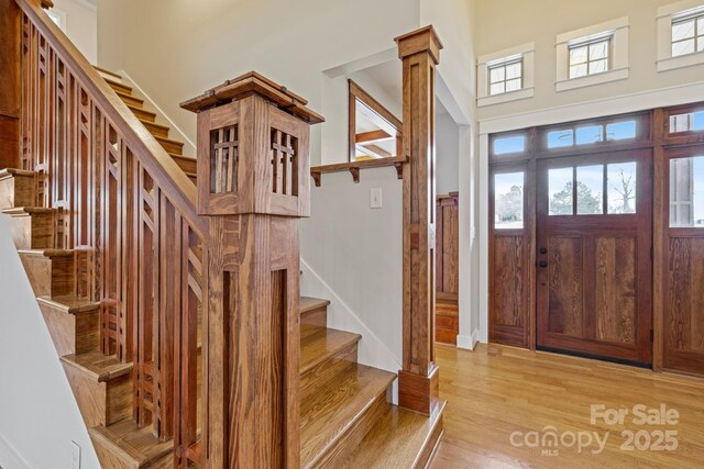 entrance foyer with a towering ceiling, a healthy amount of sunlight, decorative columns, and light hardwood / wood-style flooring