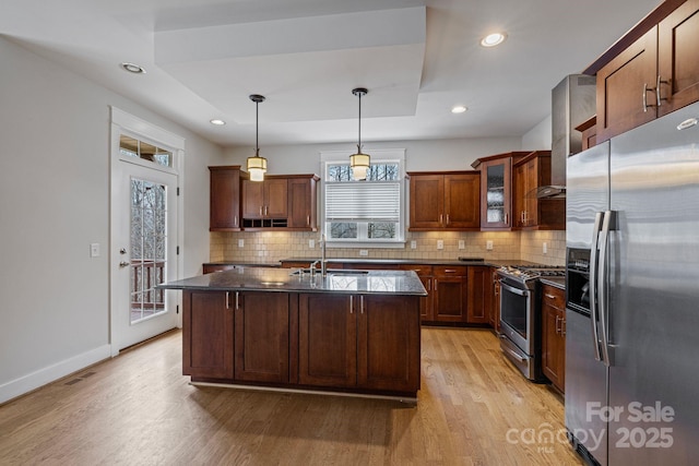 kitchen featuring stainless steel appliances, pendant lighting, a center island with sink, and light wood-type flooring