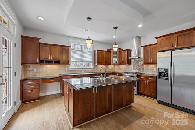 kitchen with wall chimney exhaust hood, sink, a center island with sink, pendant lighting, and stainless steel appliances