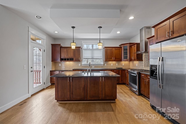 kitchen featuring decorative light fixtures, sink, a kitchen island with sink, stainless steel appliances, and wall chimney range hood