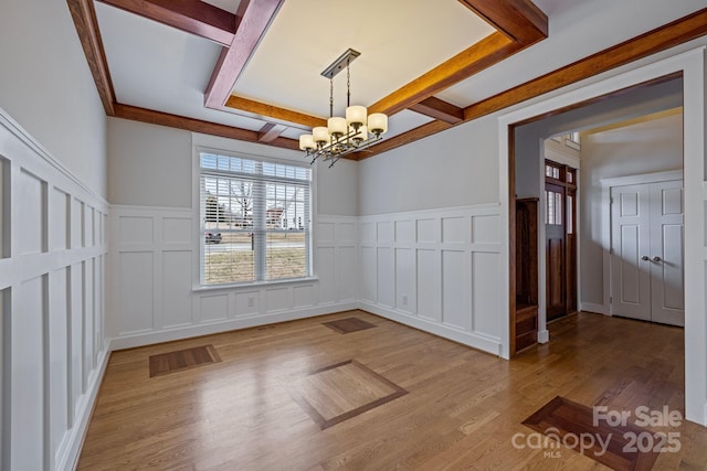 unfurnished dining area featuring hardwood / wood-style flooring, coffered ceiling, beam ceiling, and an inviting chandelier