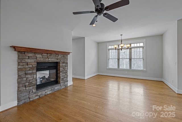 unfurnished living room with ceiling fan with notable chandelier, a fireplace, and light wood-type flooring