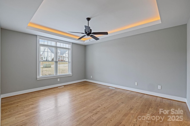 unfurnished room with ceiling fan, a raised ceiling, and light wood-type flooring