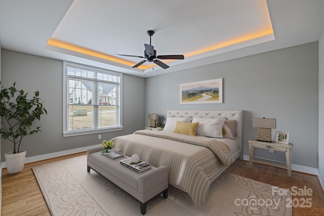 bedroom featuring ceiling fan, light wood-type flooring, and a tray ceiling