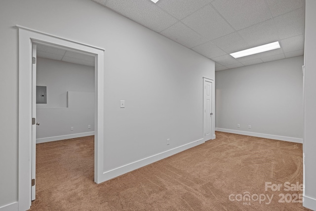 carpeted empty room featuring a drop ceiling and electric panel