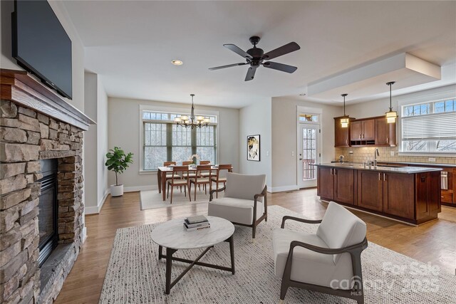 living room featuring a stone fireplace, sink, ceiling fan with notable chandelier, and light hardwood / wood-style floors