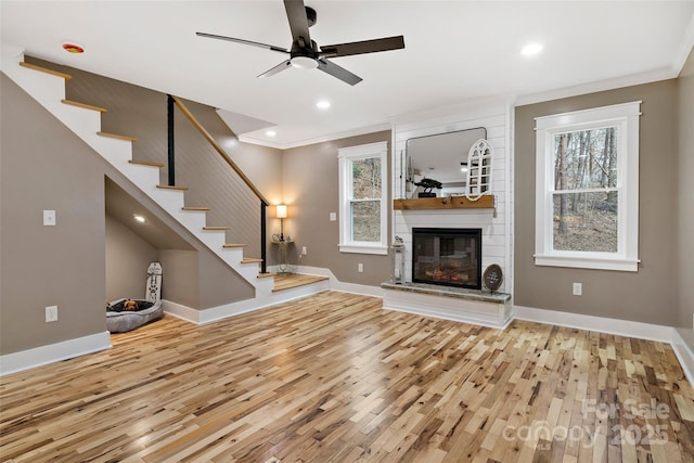 unfurnished living room featuring a healthy amount of sunlight, ceiling fan, stairway, ornamental molding, and wood finished floors