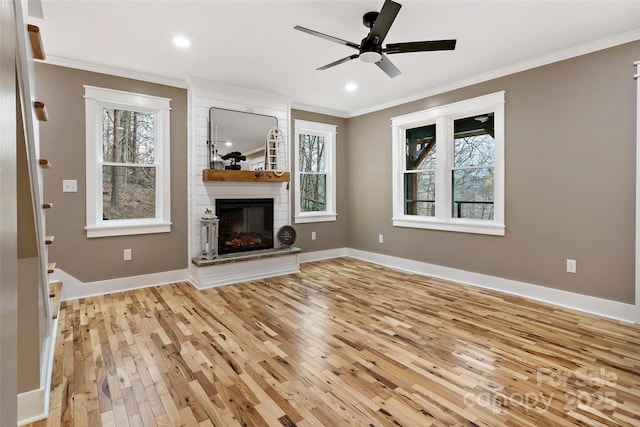 unfurnished living room with light wood finished floors, a large fireplace, baseboards, ceiling fan, and ornamental molding