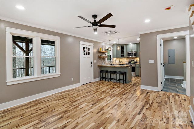 unfurnished living room featuring visible vents, baseboards, electric panel, light wood-style floors, and crown molding