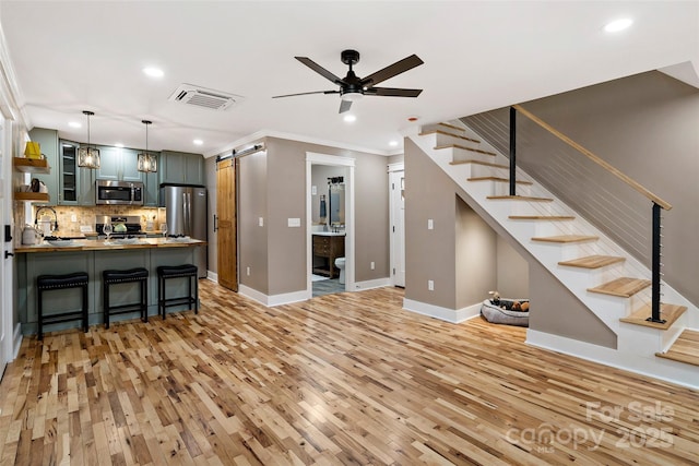 interior space with visible vents, a ceiling fan, a barn door, stairway, and light wood finished floors