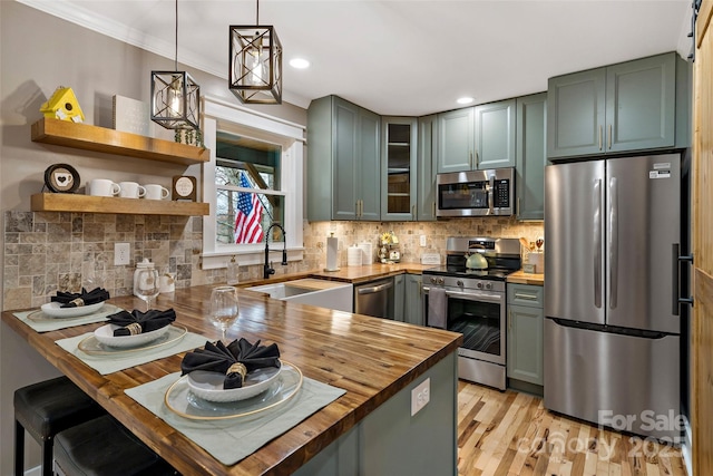 kitchen with green cabinetry, a peninsula, a sink, appliances with stainless steel finishes, and butcher block counters