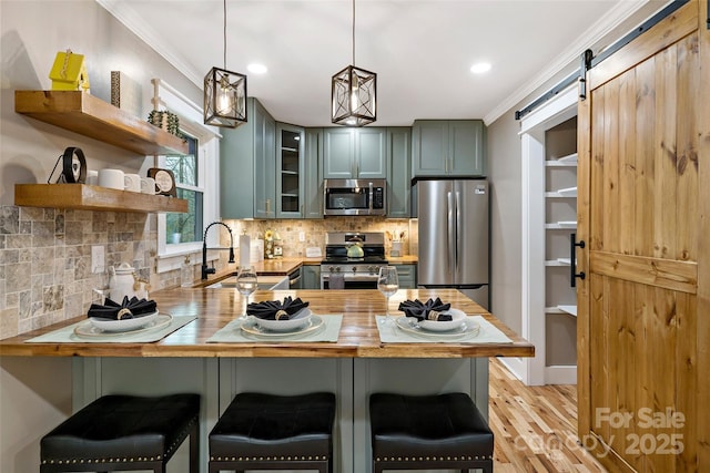 kitchen featuring a barn door, ornamental molding, appliances with stainless steel finishes, a peninsula, and a sink