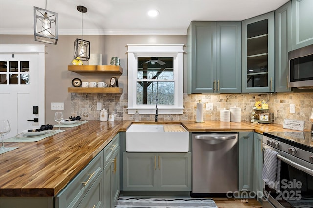 kitchen featuring butcher block countertops, stainless steel appliances, crown molding, and a sink