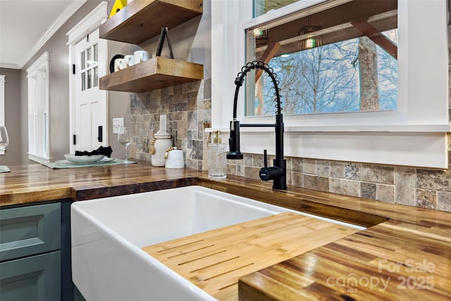 kitchen with a sink, open shelves, ornamental molding, and butcher block countertops