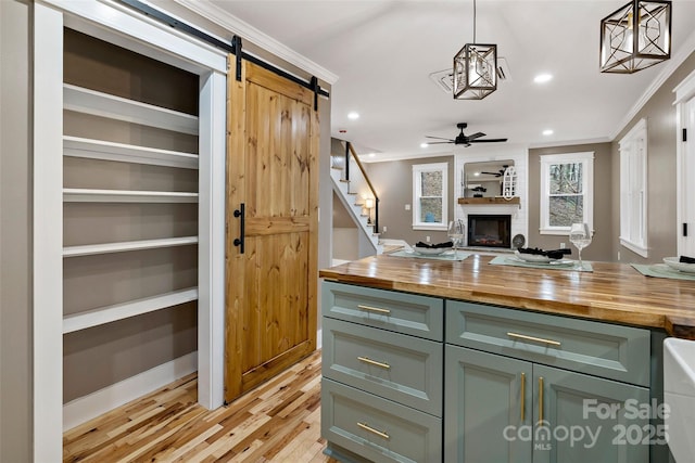 kitchen featuring butcher block countertops, crown molding, a large fireplace, and a barn door