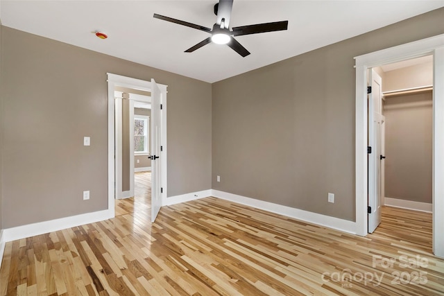 unfurnished bedroom with a spacious closet, light wood-style flooring, baseboards, and ceiling fan