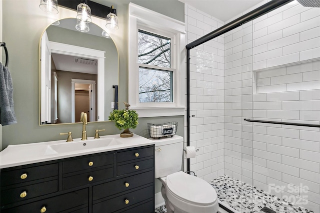 bathroom with visible vents, toilet, vanity, and a tile shower