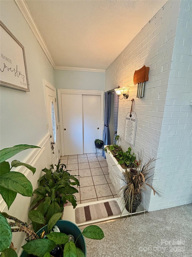 foyer entrance with light tile patterned floors, ornamental molding, a textured ceiling, and brick wall