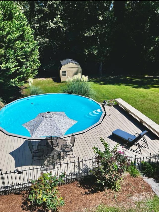 view of swimming pool featuring a storage shed, a lawn, and a deck