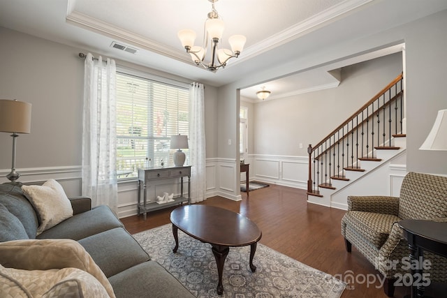 living room with a raised ceiling, crown molding, dark wood-type flooring, and a chandelier