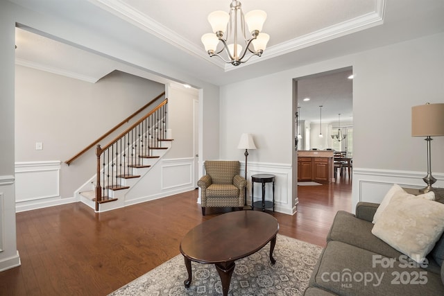 living room featuring an inviting chandelier, ornamental molding, dark hardwood / wood-style floors, and a raised ceiling