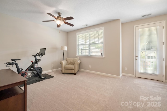 exercise area featuring ceiling fan, light colored carpet, and a textured ceiling