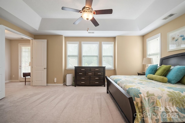 bedroom with light colored carpet, a raised ceiling, and ceiling fan