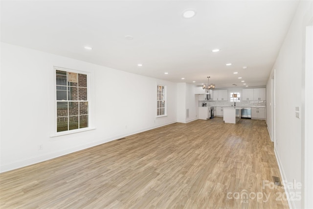 unfurnished living room featuring an inviting chandelier and light hardwood / wood-style flooring