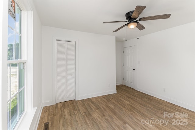 unfurnished bedroom with ceiling fan, multiple windows, wood-type flooring, and a closet